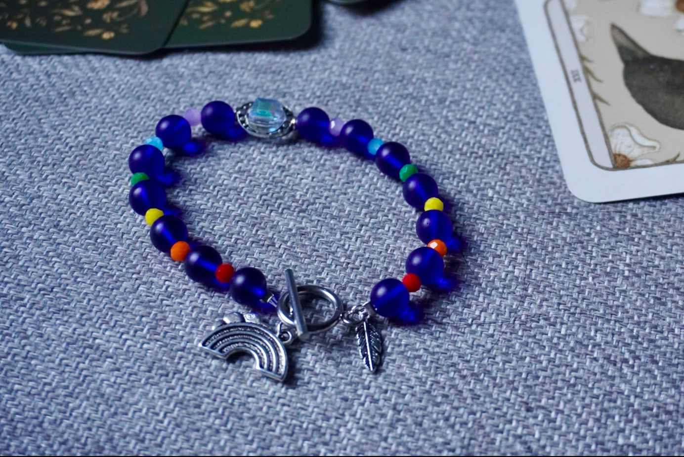 Blue beaded bracelet with charms on a textured surface with cards in the background