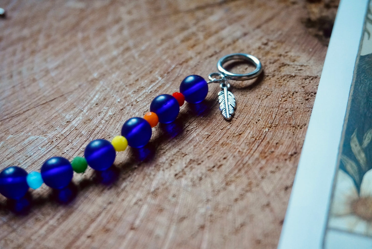 Colorful beaded bracelet with a silver toned feather charm on a wooden surface